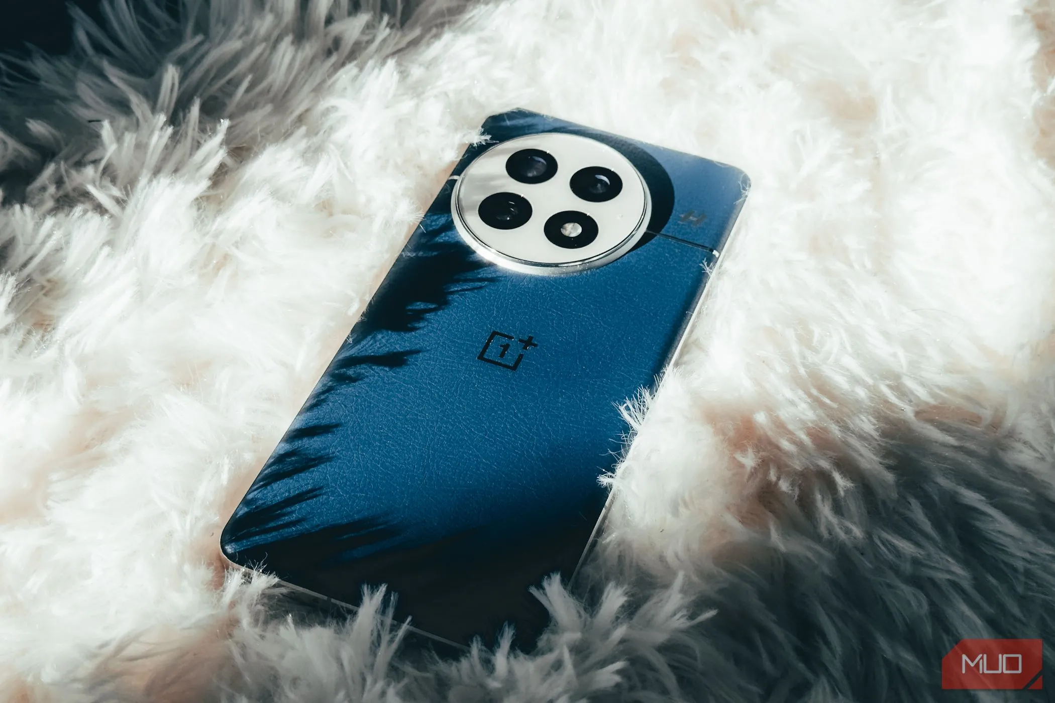 Điện thoại OnePlus 13 màu xanh Midnight Ocean đặt trên thảm lông trắng, tôn lên mặt lưng giả da.