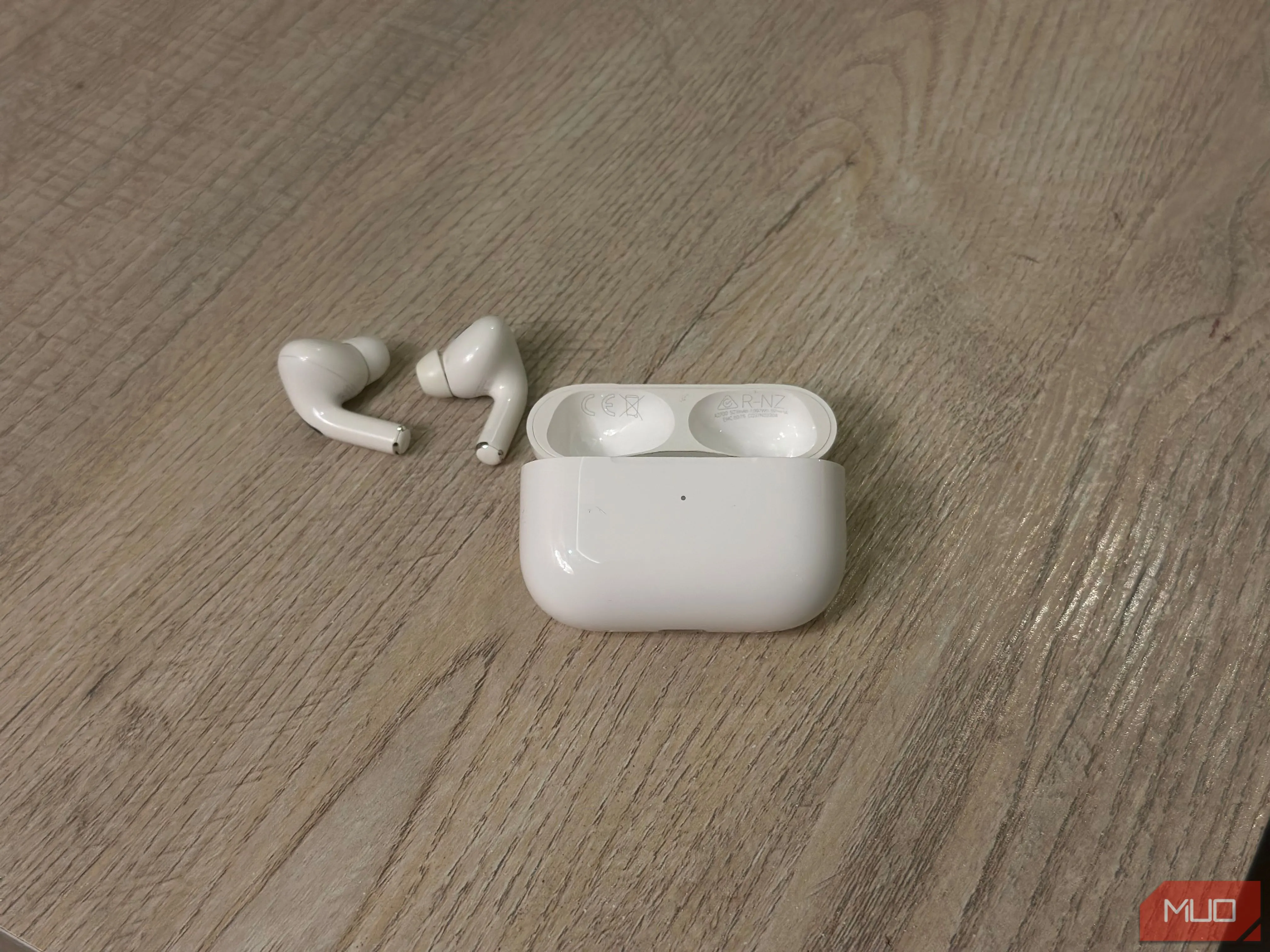 Hộp sạc AirPods và tai nghe đặt trên bàn, minh họa vị trí in số model và số serial ở mặt dưới nắp hộp sạc.