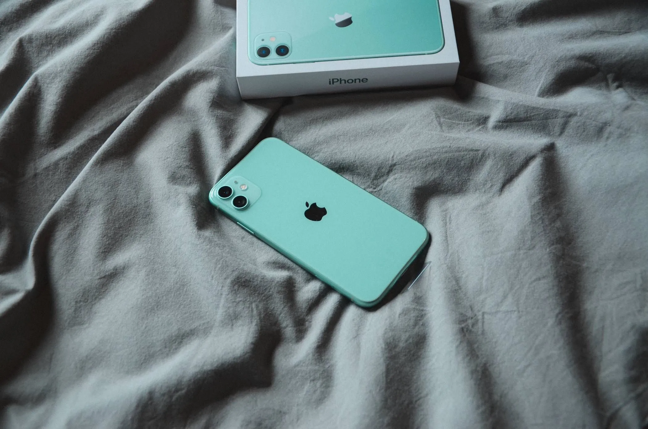 iPhone màu xanh bạc hà nằm trên chăn ga trải giường