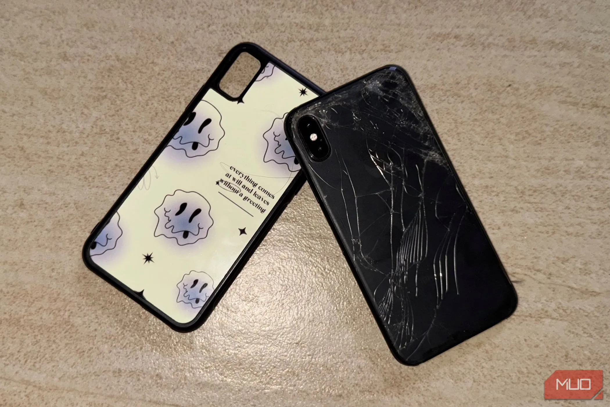 iPhone X với mặt lưng kính bị nứt nằm trên sàn nhà cùng ốp lưng, minh họa nhược điểm mặt lưng kính