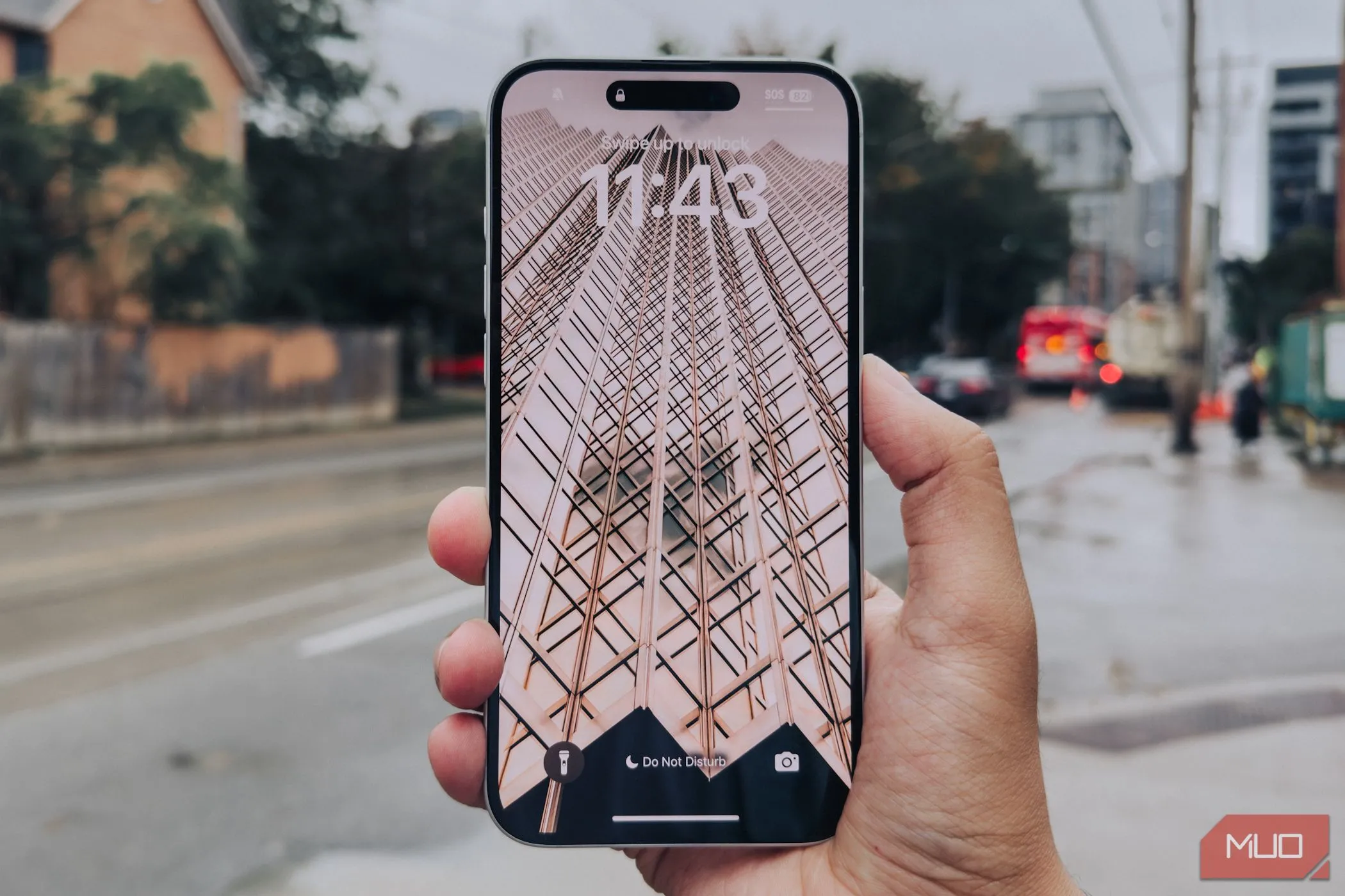 Màn hình iPhone 16 Plus đặt nghiêng trên tay với hậu cảnh thành phố, thể hiện viền màn hình mỏng