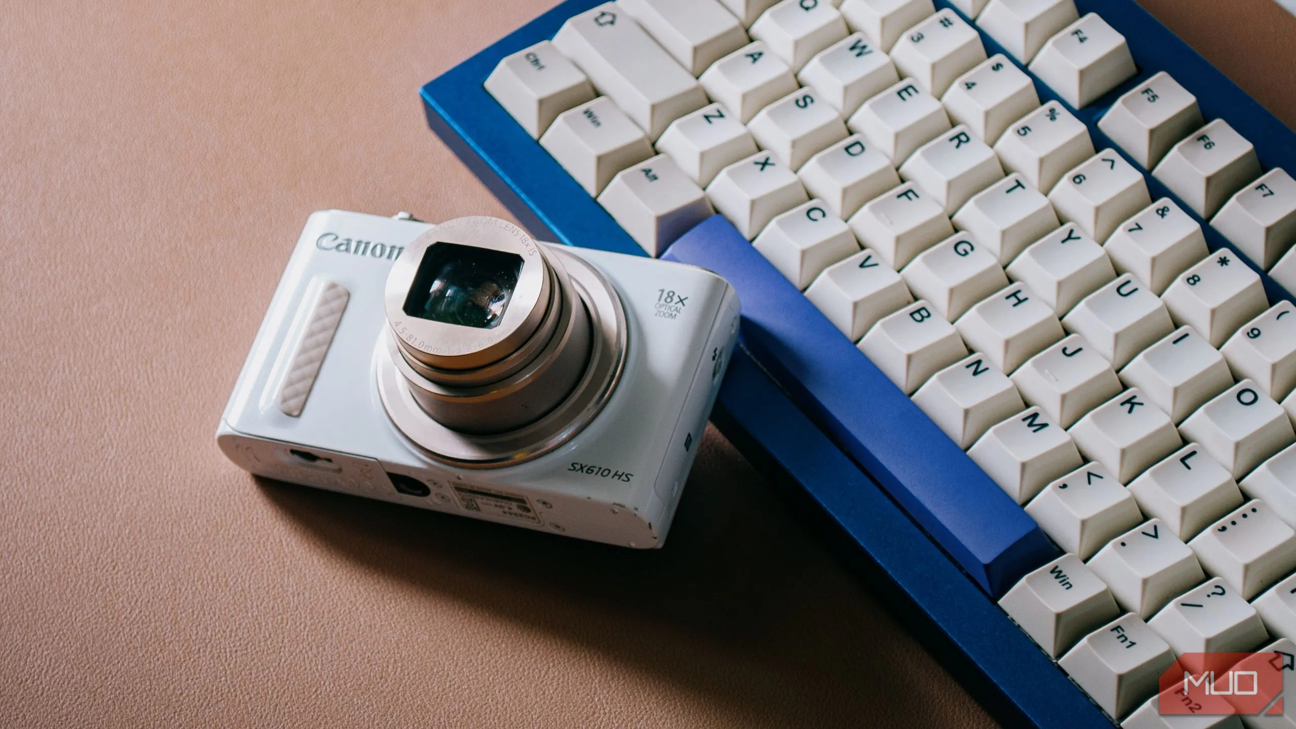 Máy ảnh compact kỹ thuật số (digicam) với ống kính đang mở, đặt trên bàn phím máy tính