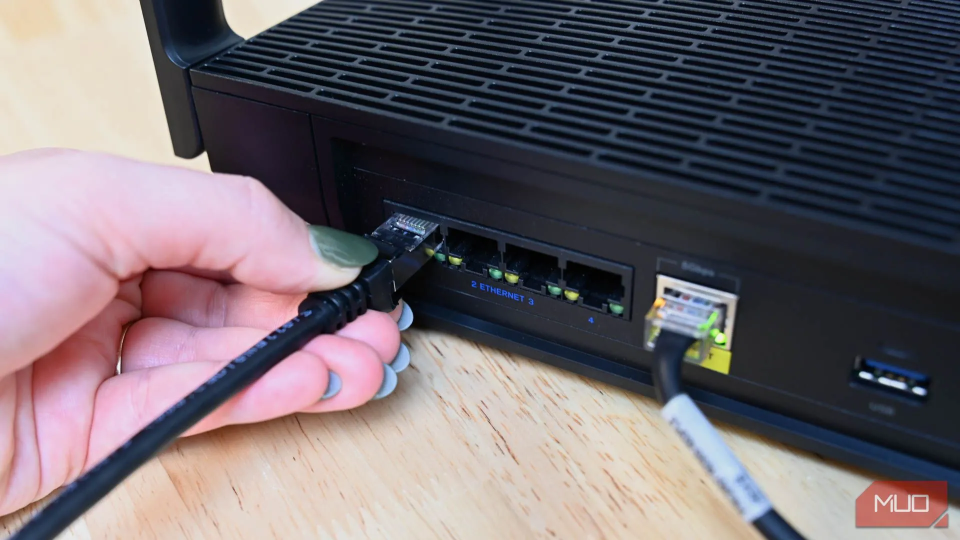 Một người dùng đang cắm cáp Ethernet vào cổng mạng trên bộ định tuyến, thể hiện việc ưu tiên kết nối có dây để tăng tốc độ internet.