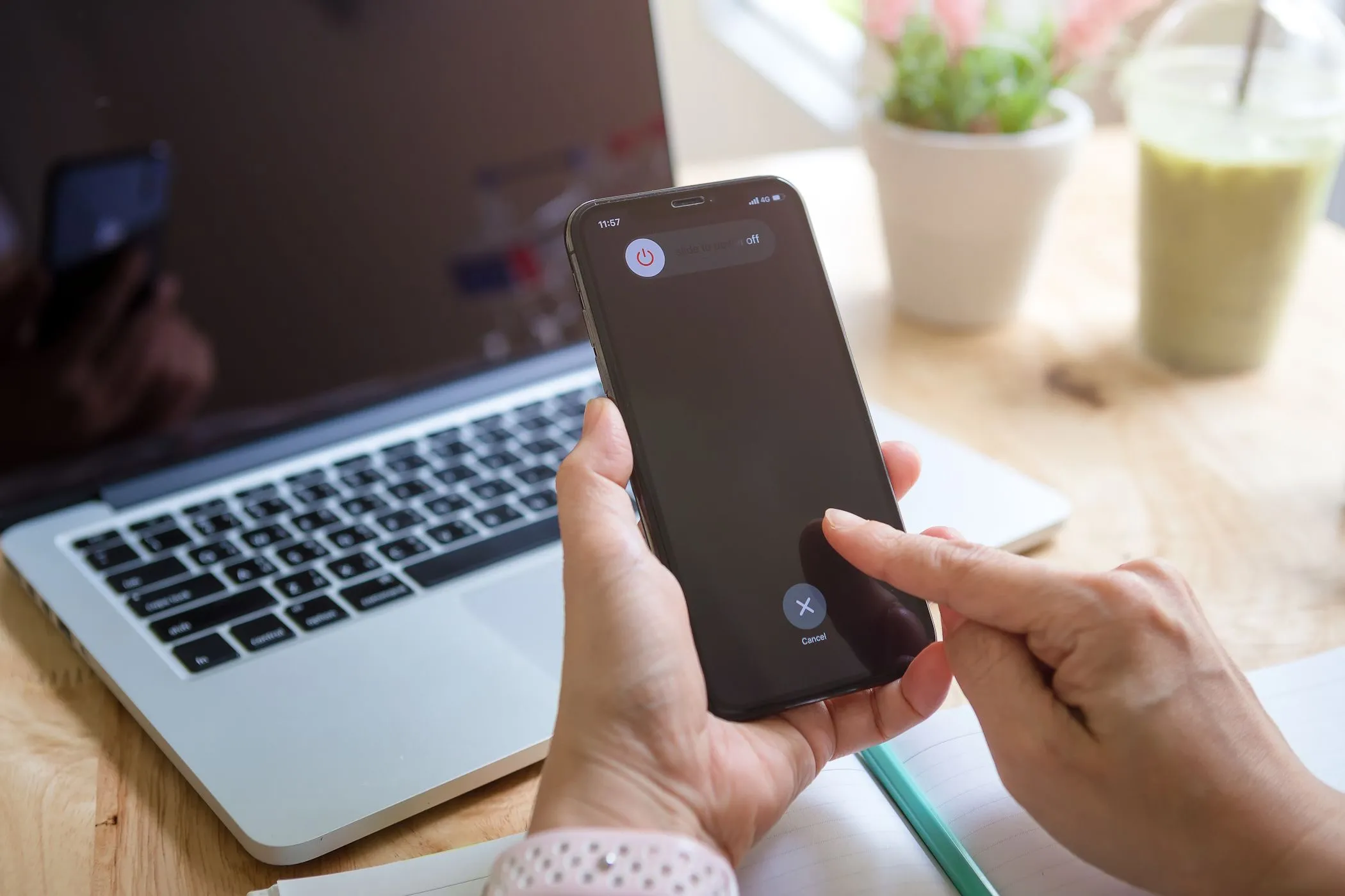 Một người phụ nữ đang cố gắng tắt iPhone của mình, có MacBook ở hậu cảnh